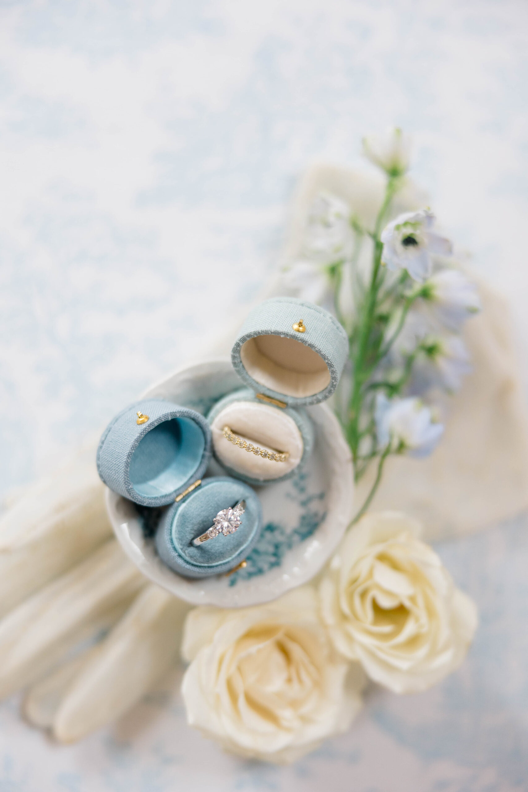 Newport Wedding Photographer and Videographer | Serving CT, RI, Massachusetts, and Surrounding New England Areas | Dusty blue flat lay with wedding rings and white florals