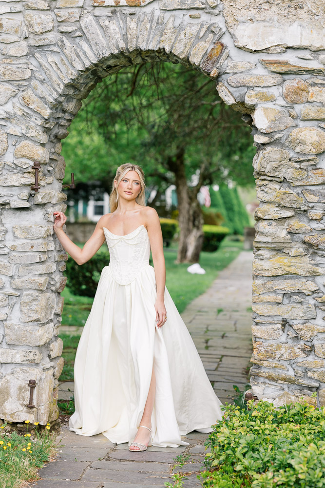 Wedding Photographer Newport RI and Wedding Videographer | Serving CT, RI, and New England Areas | Bride standing under a stone arch