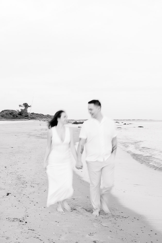 Engagement Session Newport RI and Wedding Videographer | Serving CT, RI, and New England Areas | Photo of engaged couple walking at the beach in black and white blurry film-style