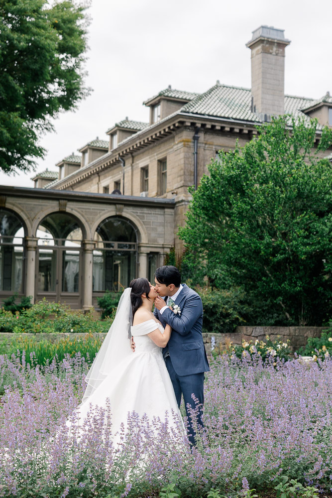 Wedding Photographers in CT and Wedding Videographer | Serving Newport, RI, and New England Areas | Bride and groom kissing in front of a mansion in the garden
