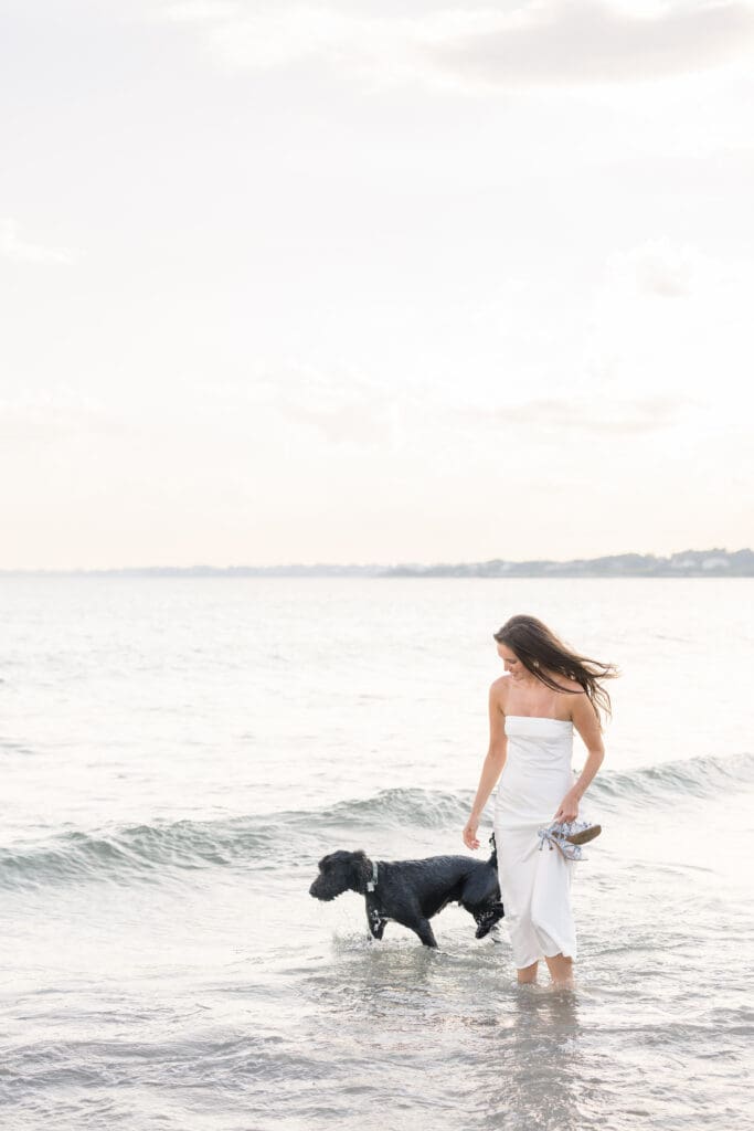 Woman walking in the ocean with her dog during a Newport engagement session.