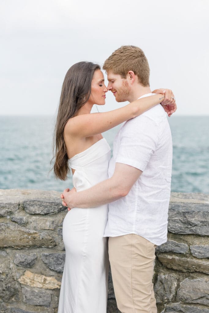 Couple embracing along a stone wall during a Newport engagement session by the ocean.